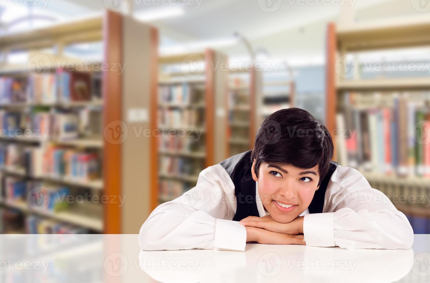giovane femmina misto gara alunno sognare ad occhi aperti nel biblioteca guardare per il sinistra. foto