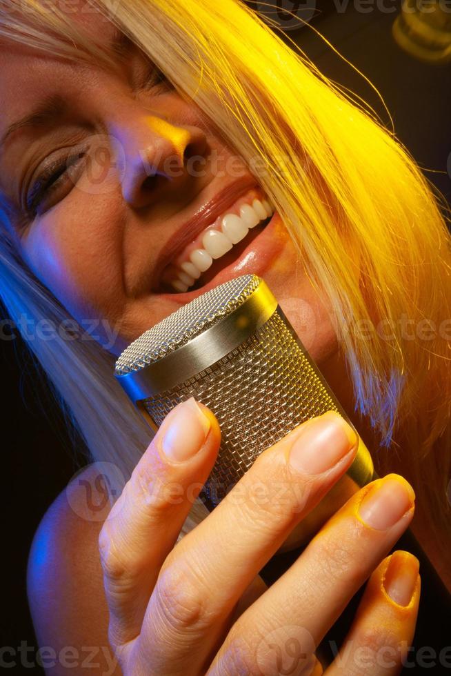 femmina cantante sotto gelificato illuminazione canta con passione in condensatore microfono. foto