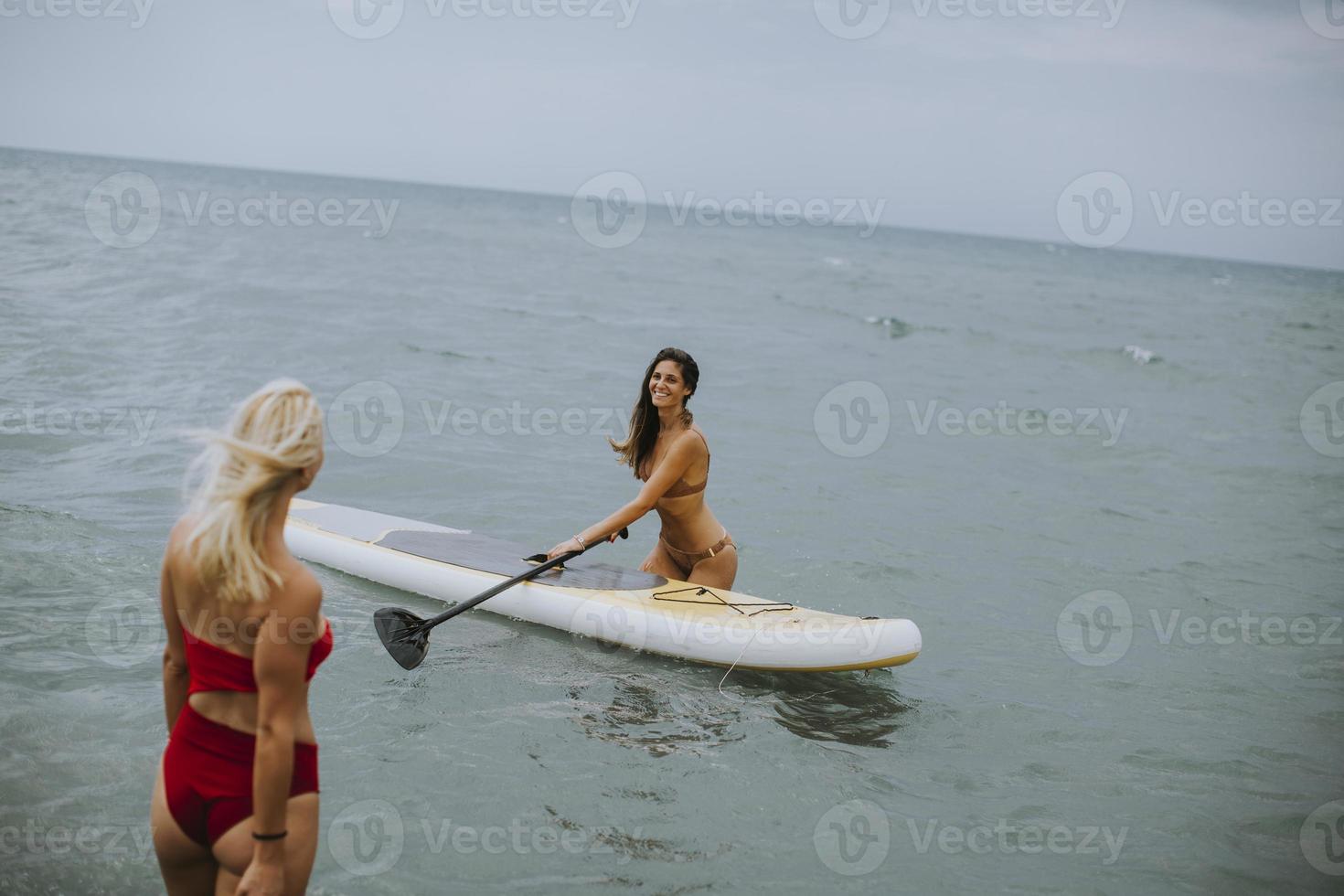 Due giovane donne con pagaia tavola nel il mare su un' estate giorno foto