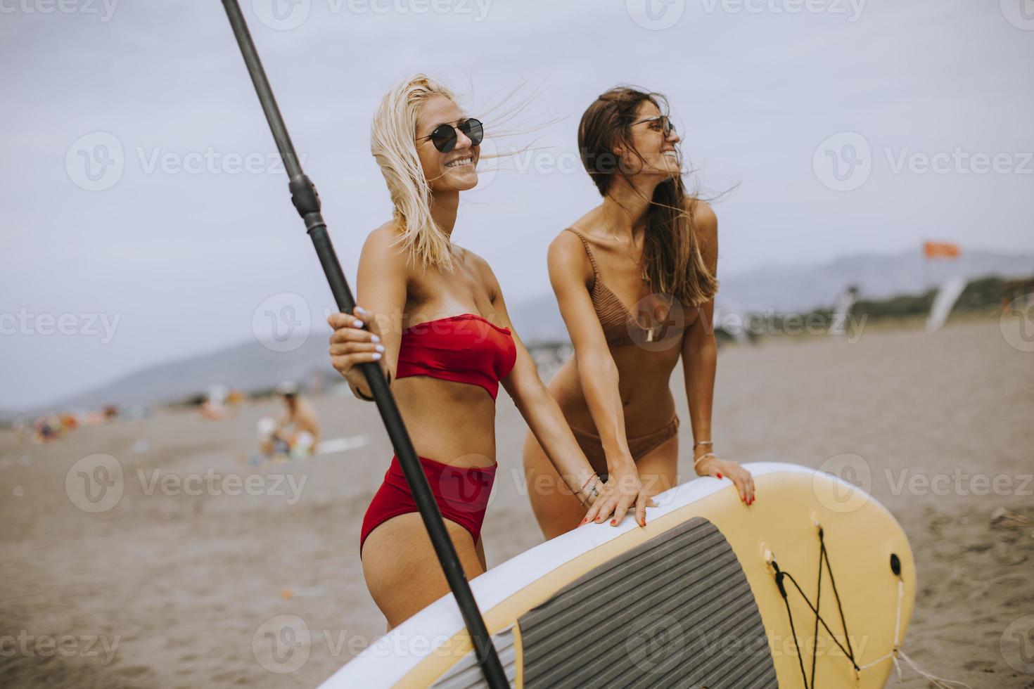 due giovani donne con paddle board sulla spiaggia in una giornata estiva foto