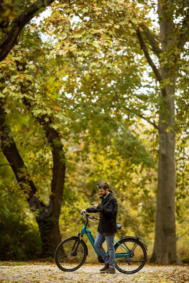 bel giovane con bicicletta elettrica nel parco autunnale foto