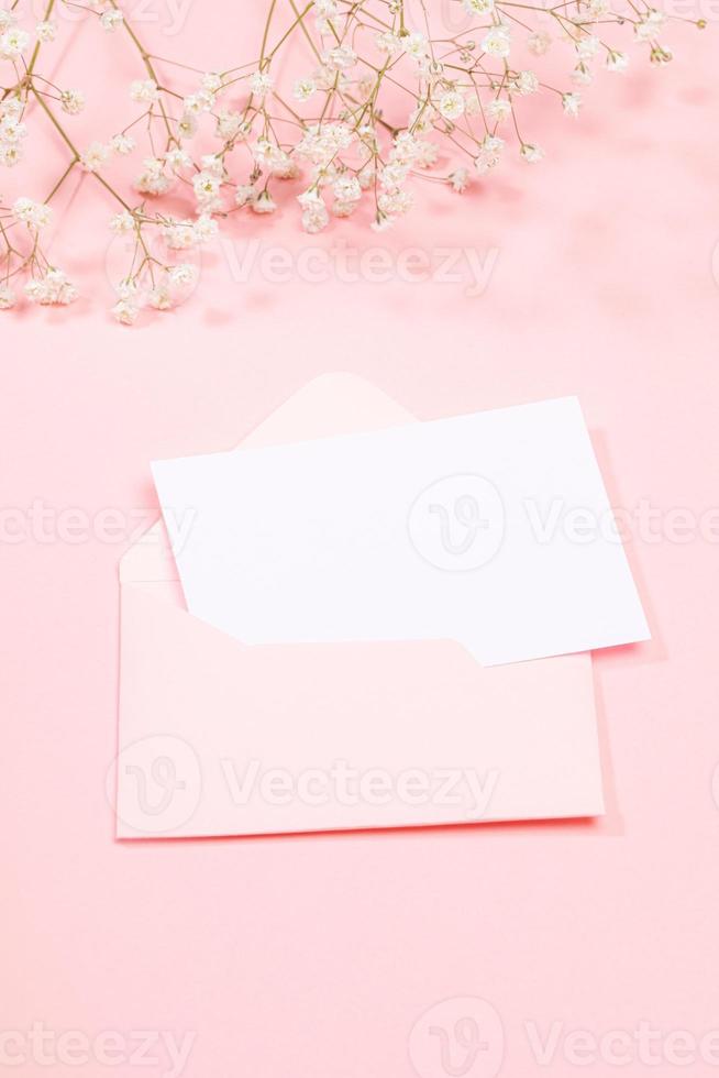pastello rosa festivo saluto carta con vuoto bianca foglio nel Busta e bianca gypsophila fiori. copia spazio per testo. foto