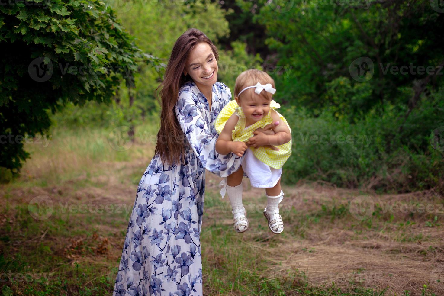 orizzontale ritratto di allegro madre giochi con sua poco bambino ragazza e sorrisi a il giardino foto