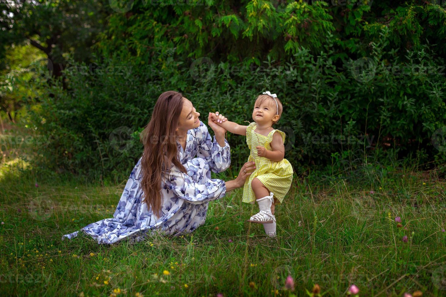 contento giovane madre giochi con sua poco figlia a il verde giardino foto