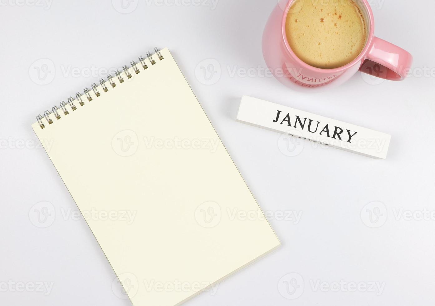 piatto posare di vuoto pagina carta taccuino, di legno calendario gennaio e rosa tazza di caffè su bianca sfondo. foto