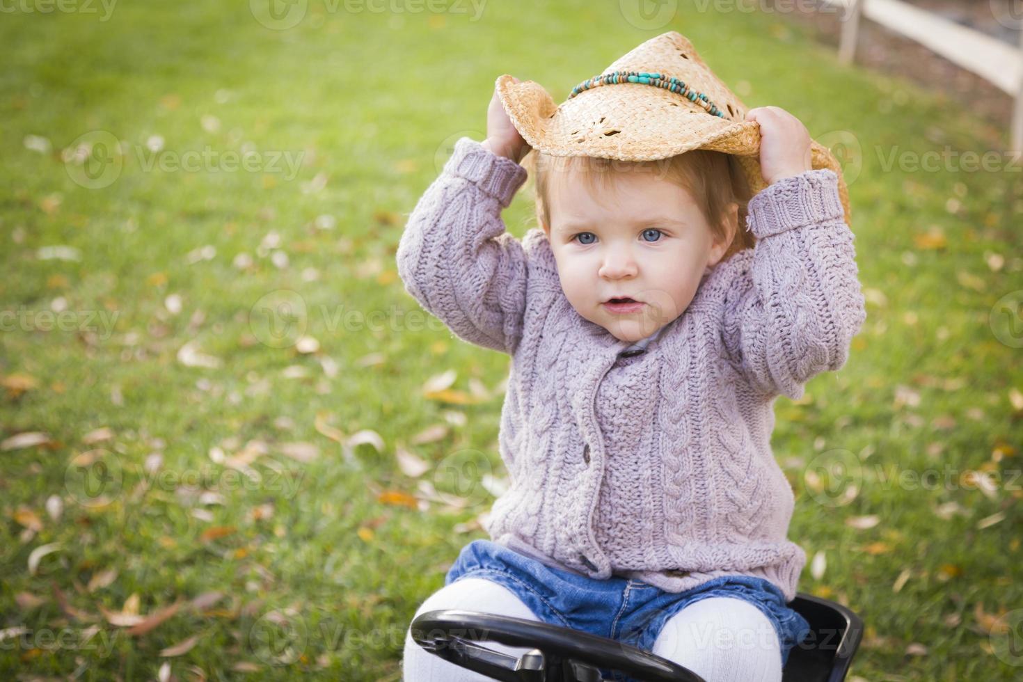 bambino piccolo indossare cowboy cappello e giocando su giocattolo trattore al di fuori foto