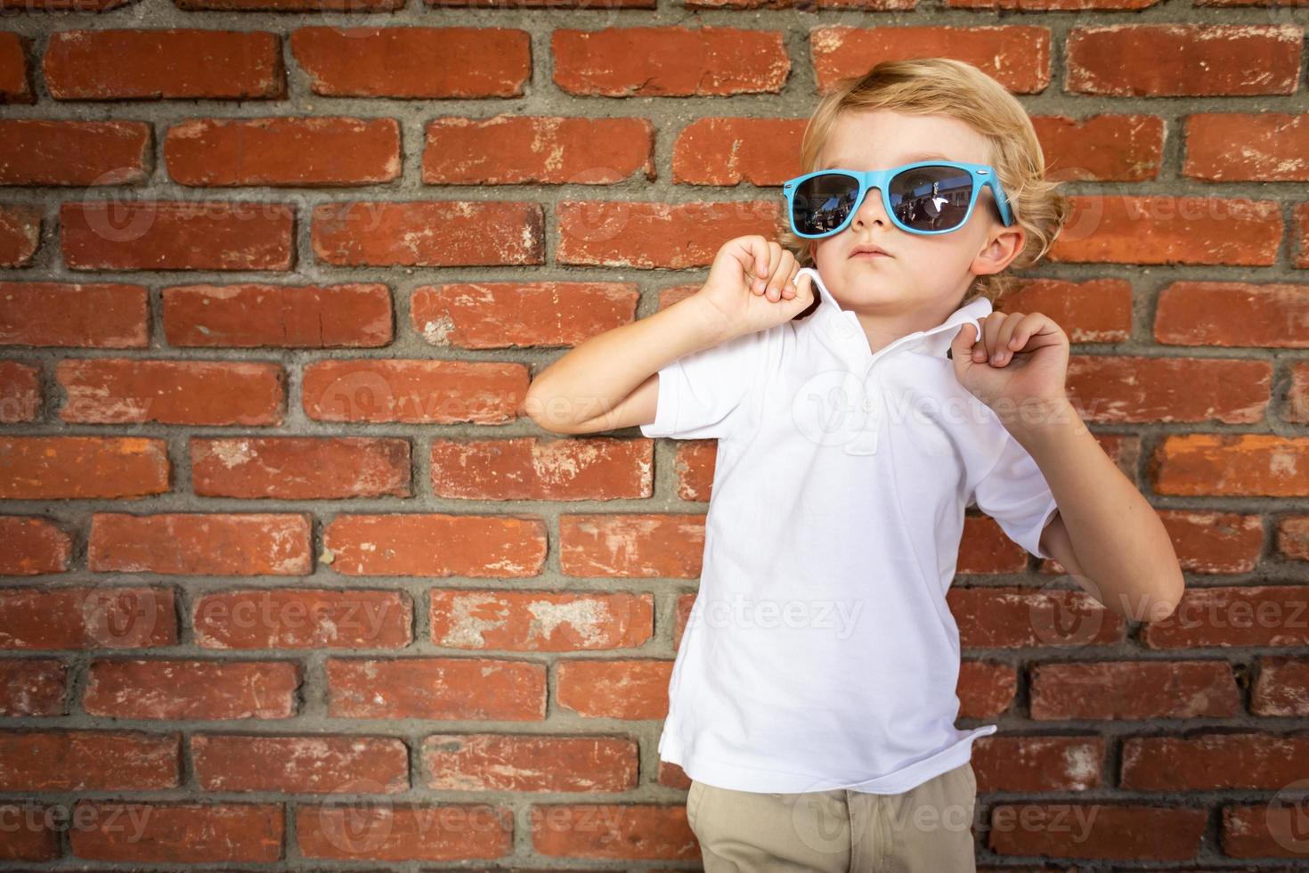 carino giovane caucasico ragazzo indossare occhiali da sole contro mattone parete foto