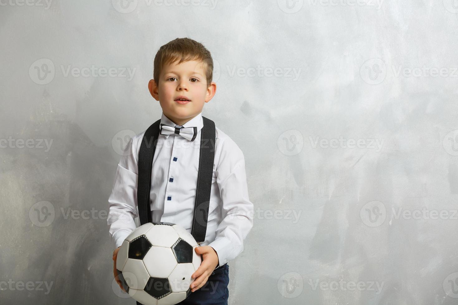 poco ragazzo con un' calcio palla su un' grigio sfondo foto