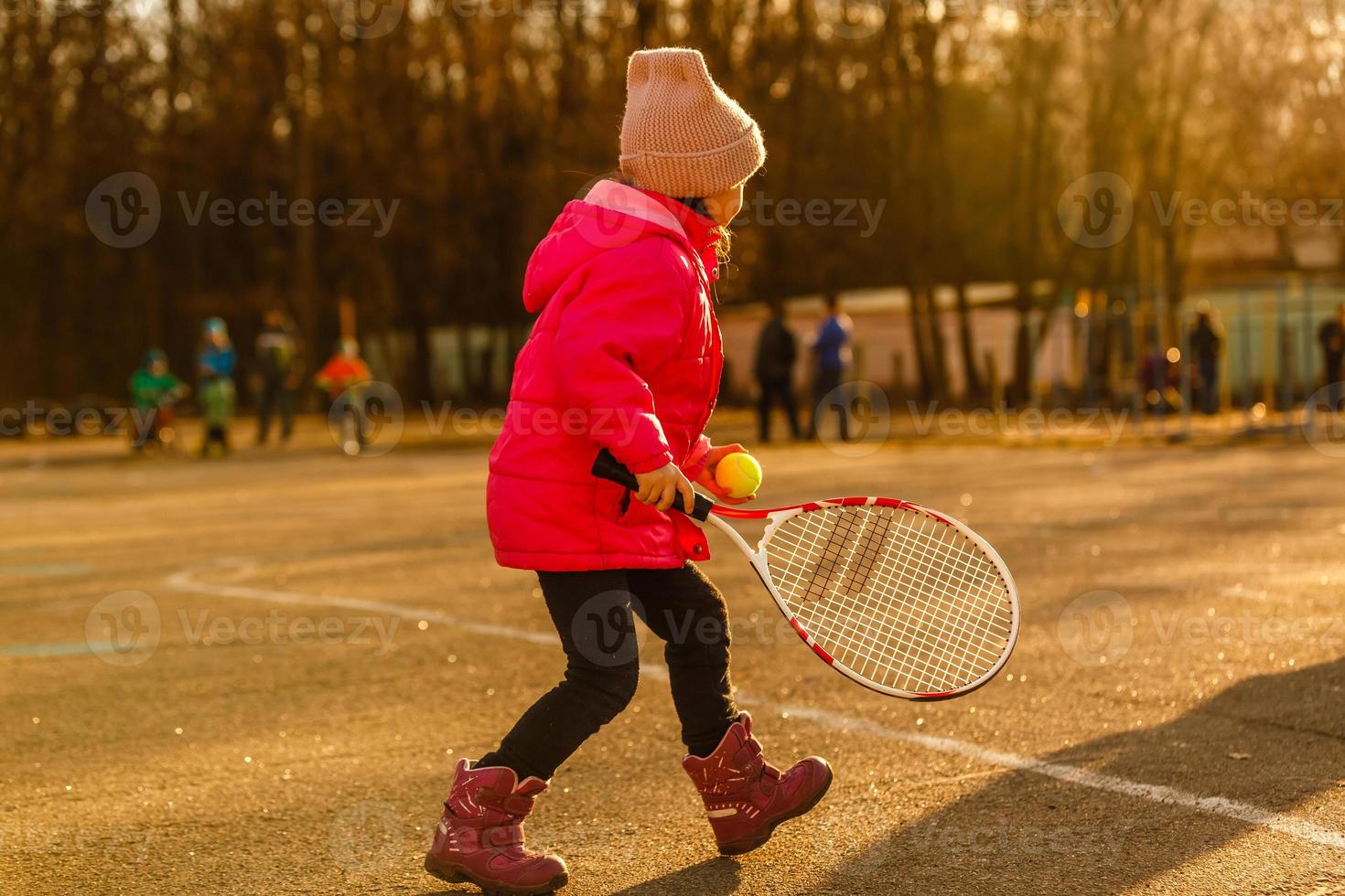 poco ragazza apprendimento per colpire il tennis sfera. poco ragazza tennis giocatore con palla e racchetta su Tribunale. attivo esercizio per bambini foto