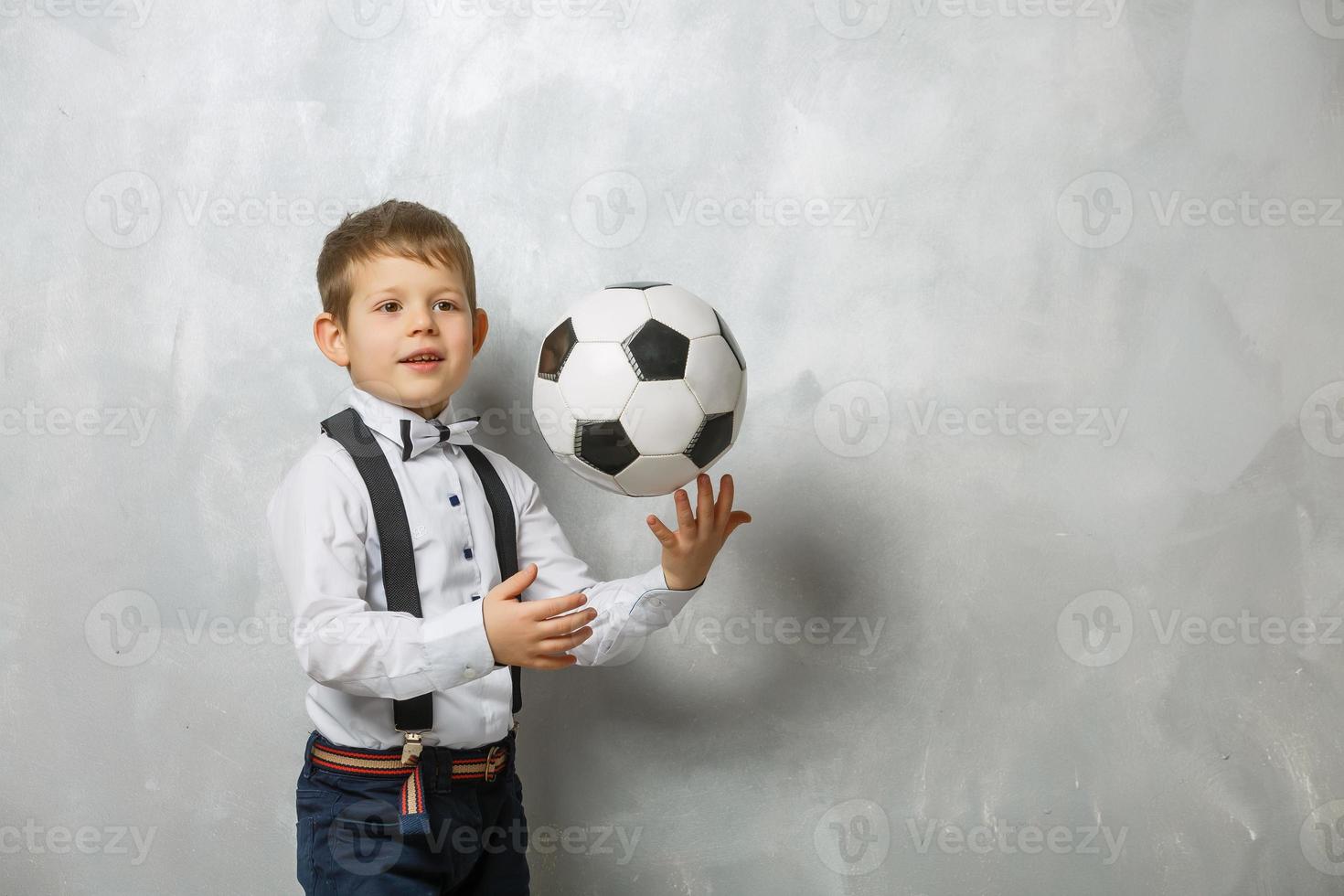 poco ragazzo con un' calcio palla su un' grigio sfondo foto