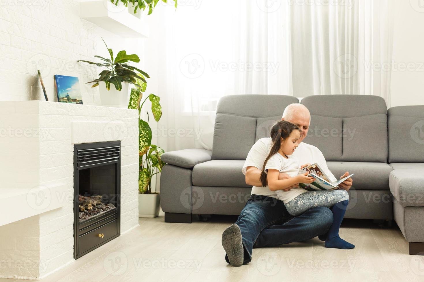 contento poco ragazza con nonno lettura storia libro a casa foto