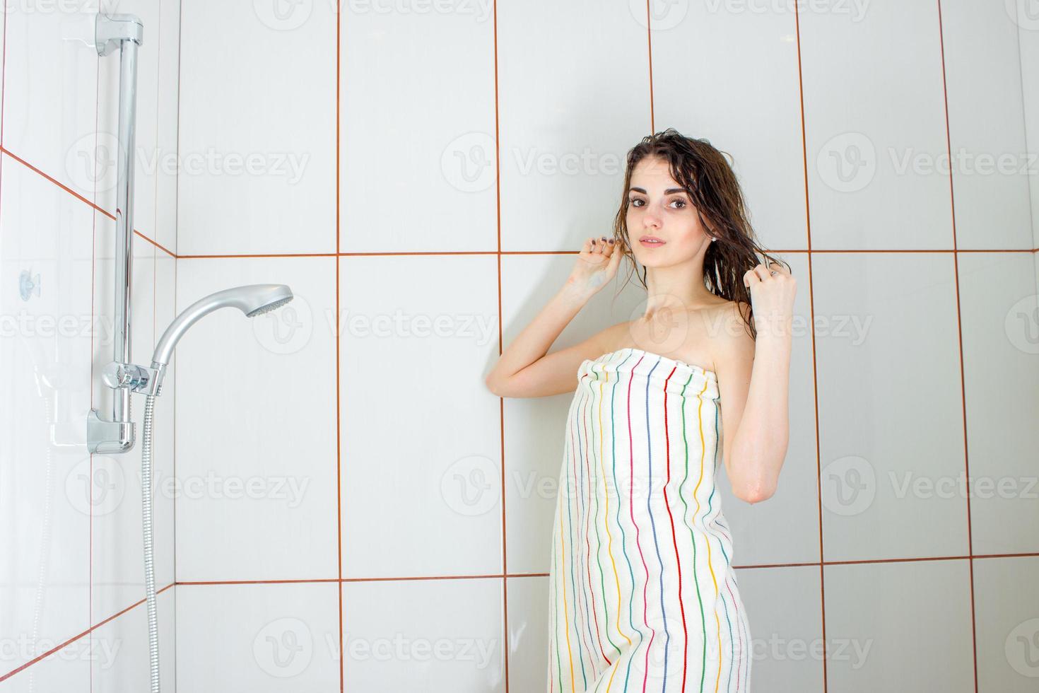 ragazza in piedi nel un' vasca da bagno nel un' grande asciugamano e si raddrizza capelli foto