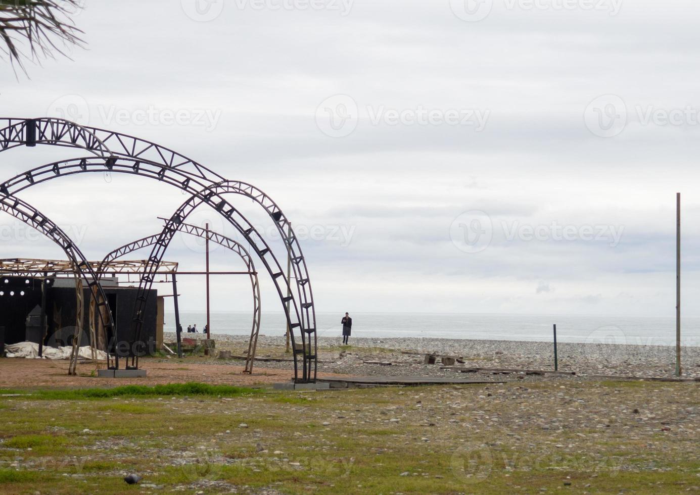 un' uomo su il riva del mare Il prossimo per un abbandonato struttura. telaio di arrugginito pezzi di ferro su il spiaggia. foto