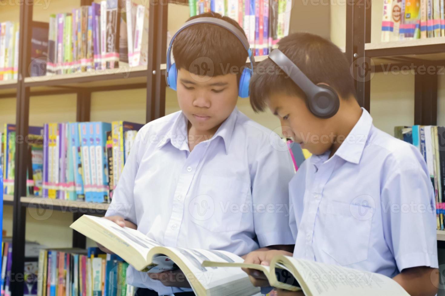 morbido fucus di Due asiatico ragazzo studenti siamo ascoltando media, lettura e consulenza di preferito libro a biblioteca di scuola foto