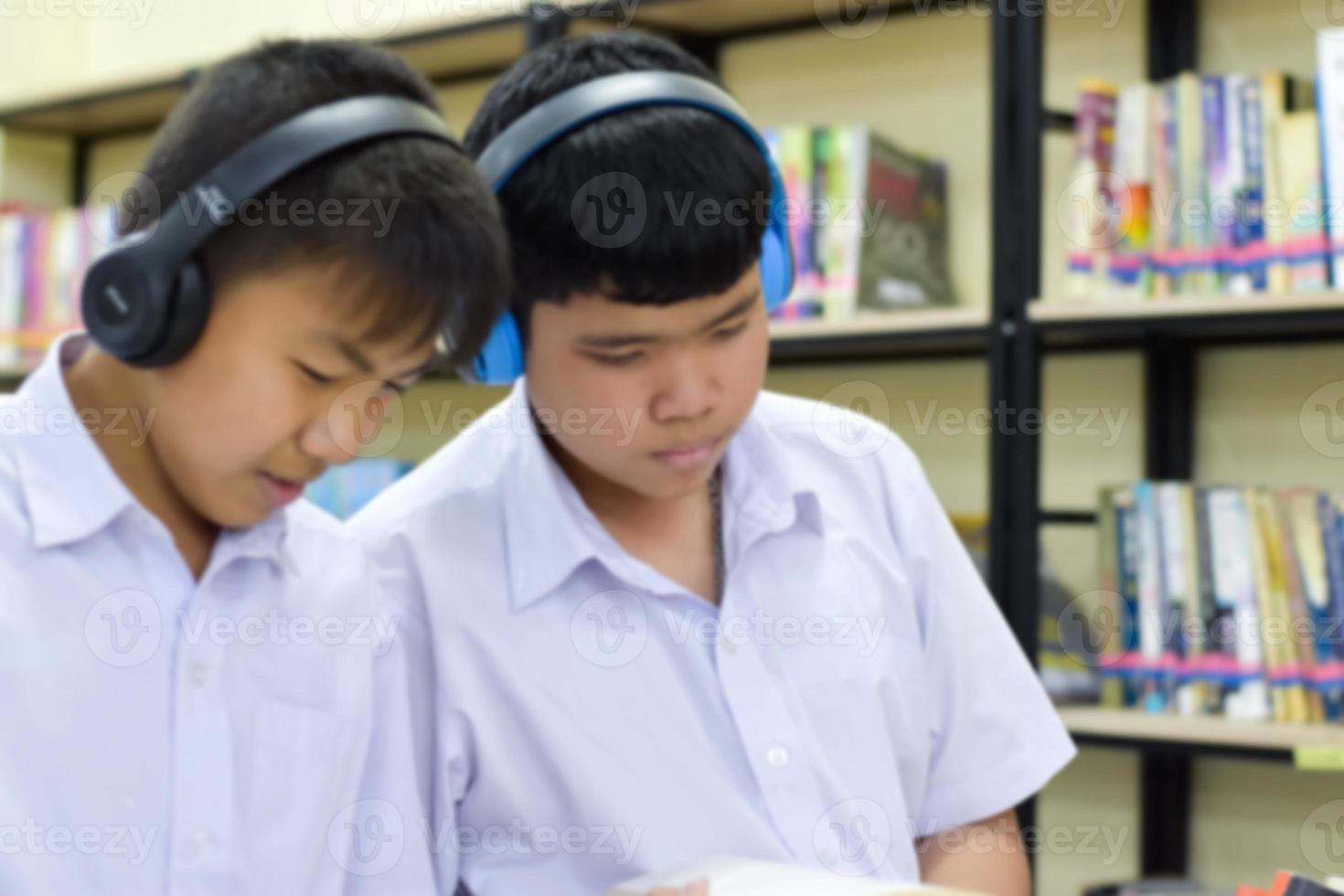 morbido fucus di Due asiatico ragazzo studenti siamo ascoltando media, lettura e consulenza di preferito libro a biblioteca di scuola foto