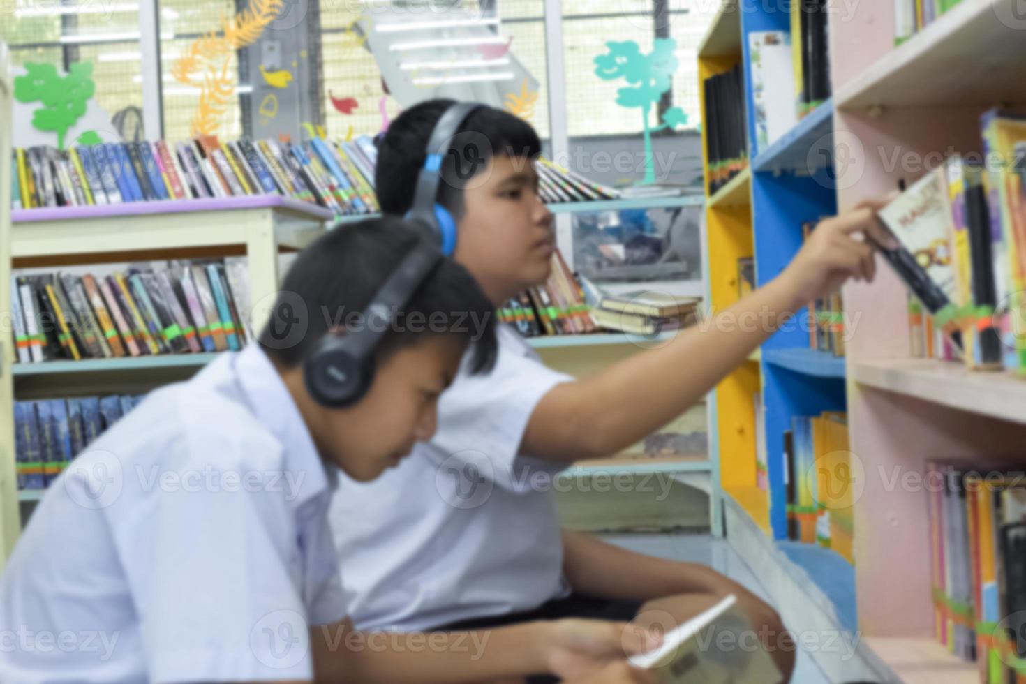 morbido fucus di Due asiatico ragazzo studenti siamo ascoltando media, lettura e consulenza di preferito libro a biblioteca di scuola foto
