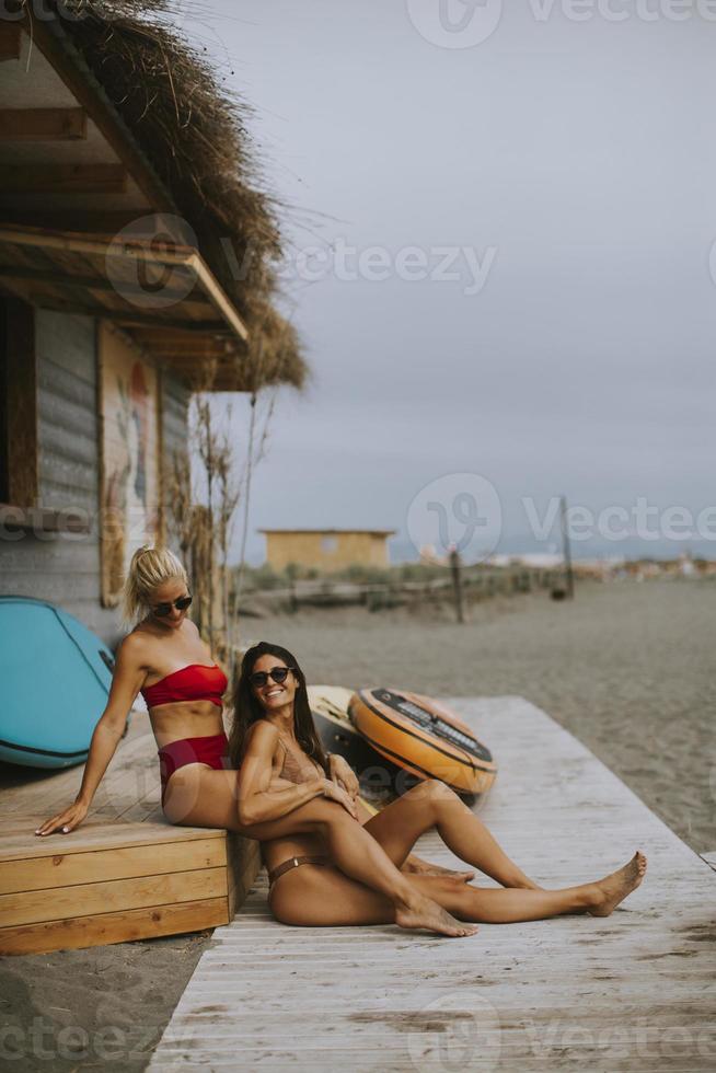 giovani donne in bikini seduti vicino alla cabina di surf su una spiaggia al giorno d'estate foto