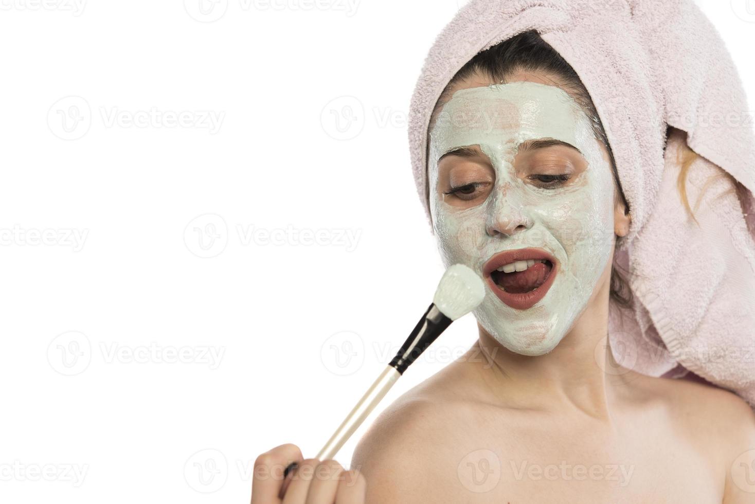 bellissimo giovane donna con asciugamano avvolto in giro sua testa l'applicazione argilla viso maschera a il bagno foto