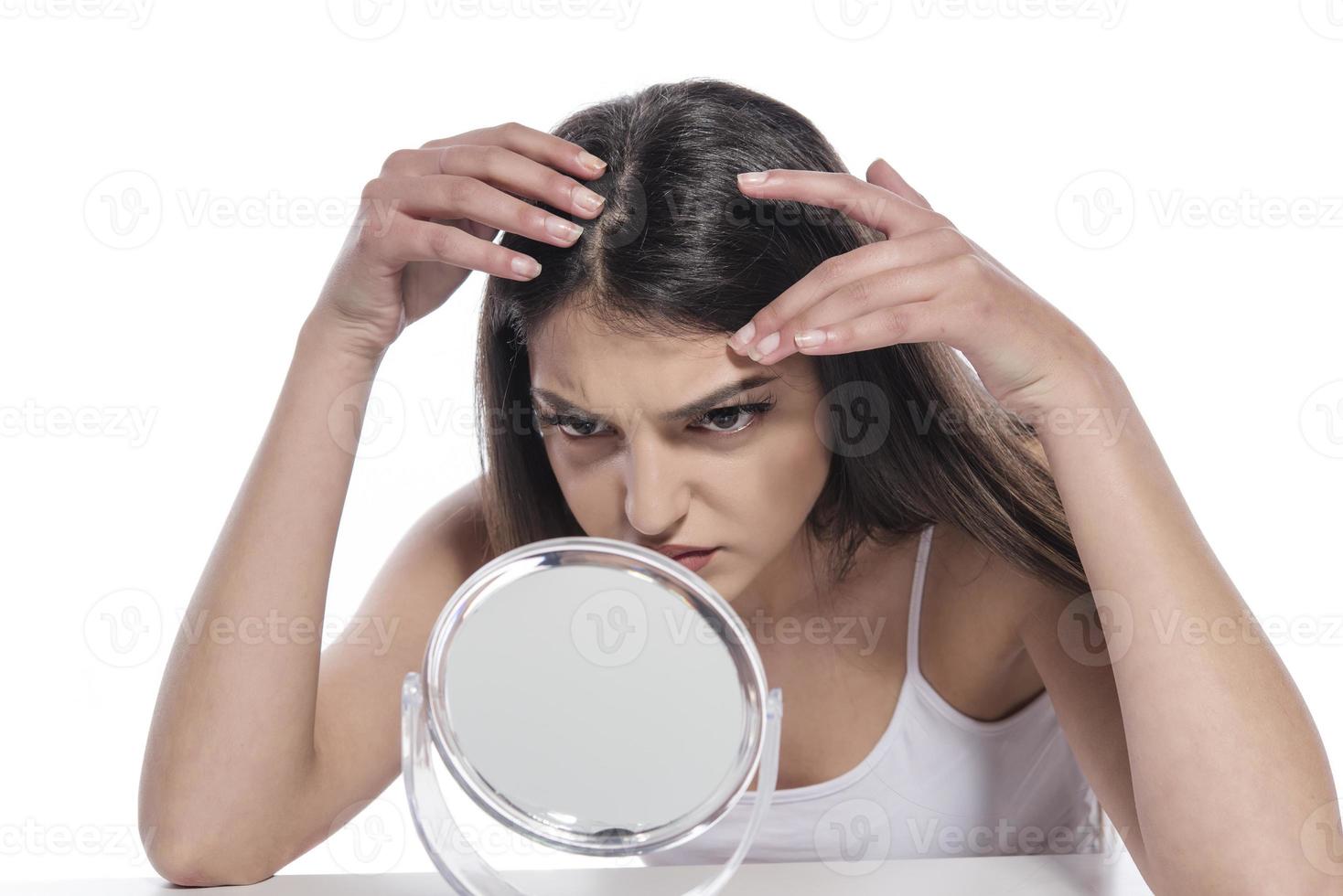 ritratto di un' ragazza mettendo cosmetico unguento su viso mentre Guardando a specchio interno foto