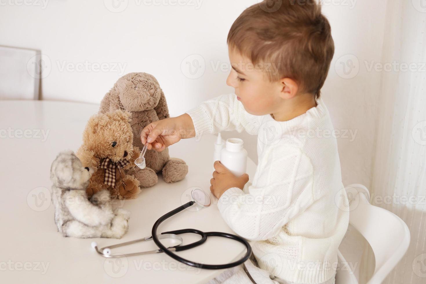 carino poco ragazzo giocando medico a casa e curare felpa giocattolo. dolce bambino piccolo bambino giochi interno. avendo divertimento. bambini e medicinale, assistenza sanitaria. foto