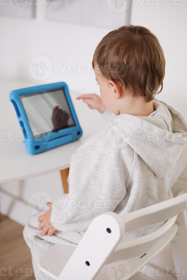 contento poco ragazzo giocando gioco su digitale tavoletta a casa. ritratto di un' bambino a casa Guardando cartone animato su il tavoletta. moderno ragazzo e formazione scolastica tecnologia. foto