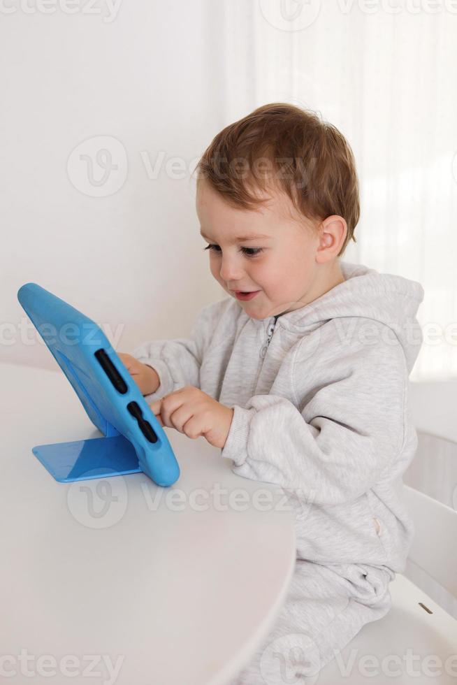 contento poco ragazzo giocando gioco su digitale tavoletta a casa. ritratto di un' bambino a casa Guardando cartone animato su il tavoletta. moderno ragazzo e formazione scolastica tecnologia. foto