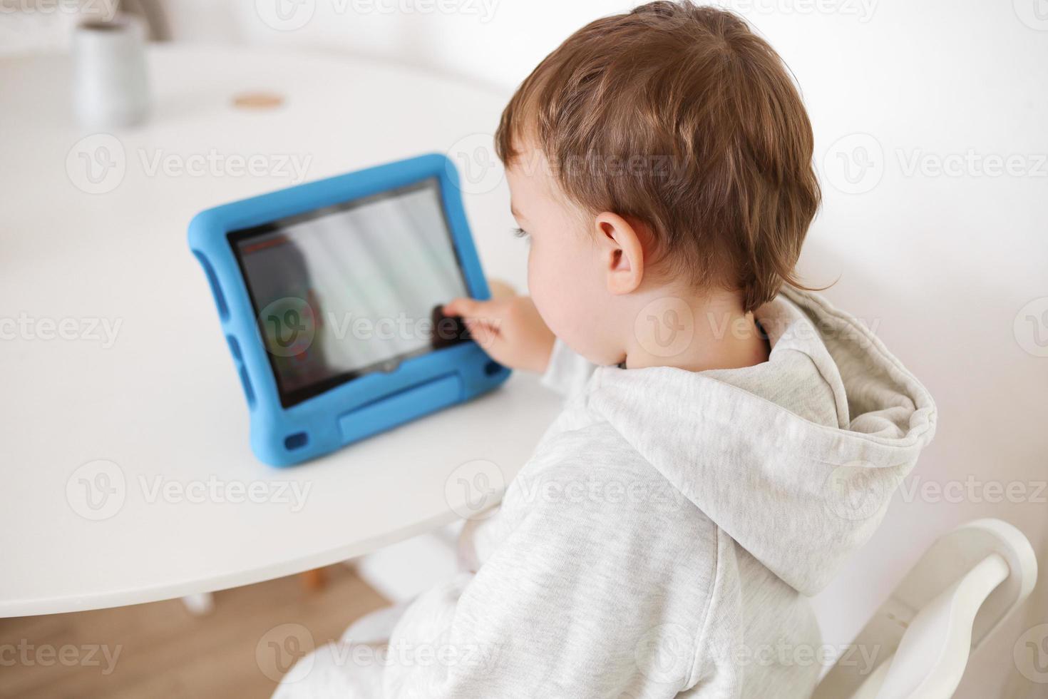 contento poco ragazzo giocando gioco su digitale tavoletta a casa. ritratto di un' bambino a casa Guardando cartone animato su il tavoletta. moderno ragazzo e formazione scolastica tecnologia. foto