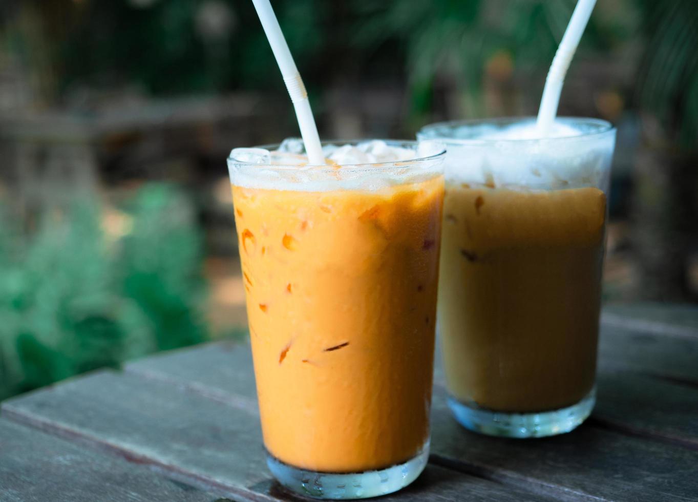 avvicinamento tailandese tè e caffè ghiaccio latte bianca su legna tavolo nel bar e albero sfondo foto