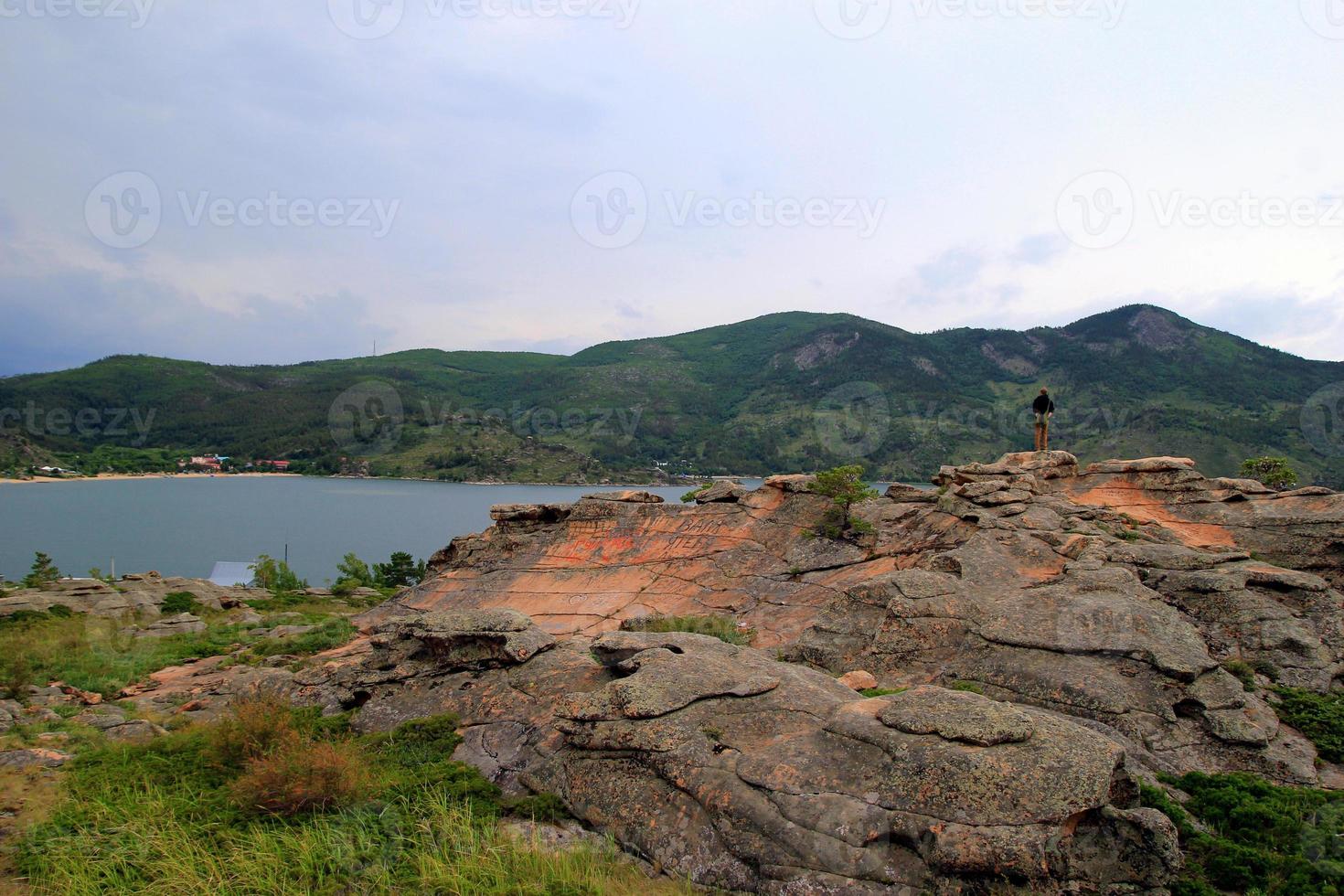 viaggio per kazakistan, bayanaul nazionale parco. il giovane uomo è guardare su il Visualizza con un' lago e montagne. foto