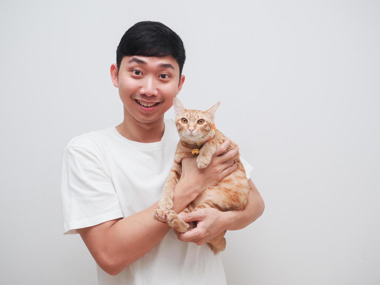 asiatico uomo bianca camicia contento Sorridi e allegro trasportare arancia gatto Guarda a telecamera su bianca sfondo foto