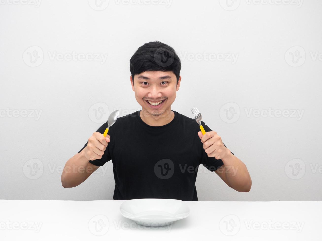 asiatico uomo Tenere posate e sorridente a il cena tavolo foto