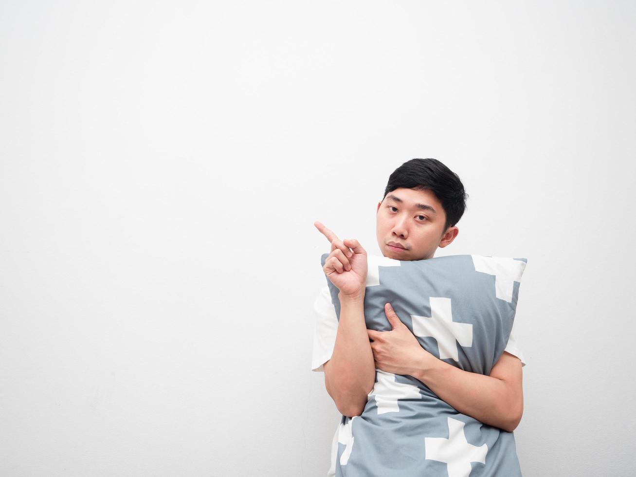 asiatico uomo abbracciare cuscino annoiato viso punto dito sinistra lato copia spazio bianca sfondo foto