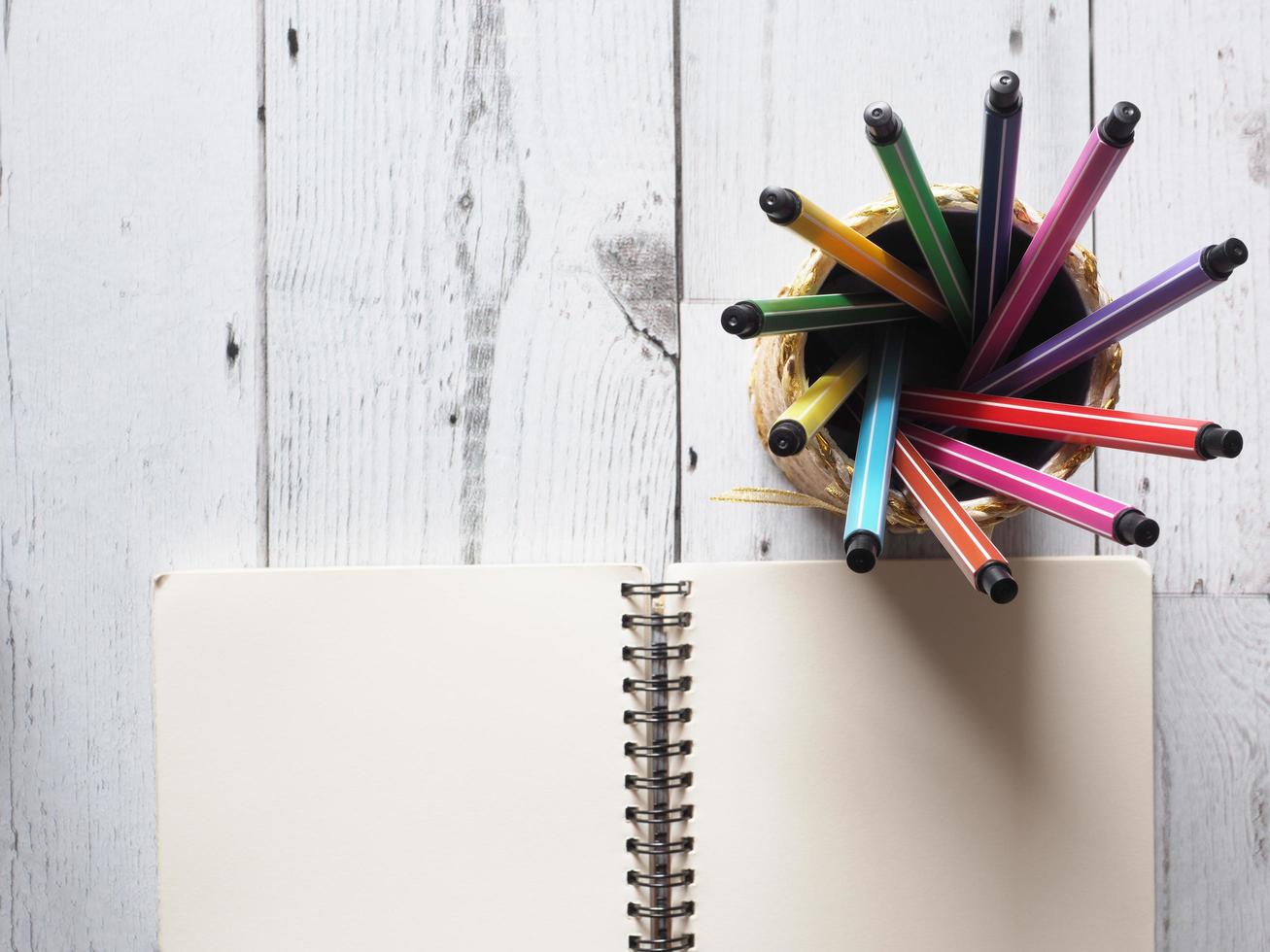 penna colorato Vettore circolare nel scatola con Aperto taccuino vuoto pagina su bianca legna tavolo e natura leggero di sole idea concetto superiore vista, affari e formazione scolastica foto