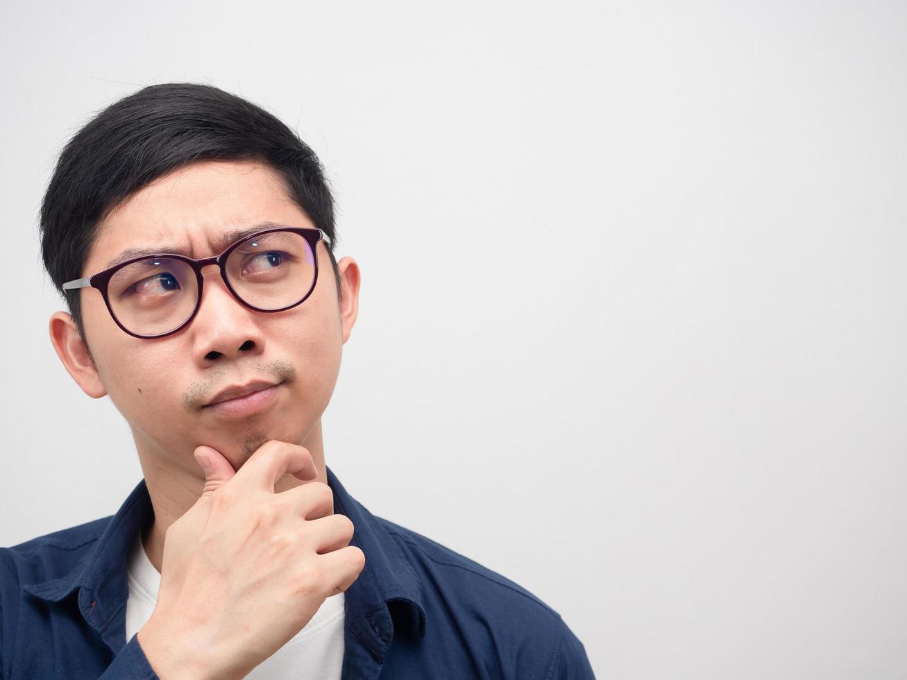 vicino su viso di asiatico uomo indossare bicchieri pensiero e guardare a copia spazio bianca sfondo foto