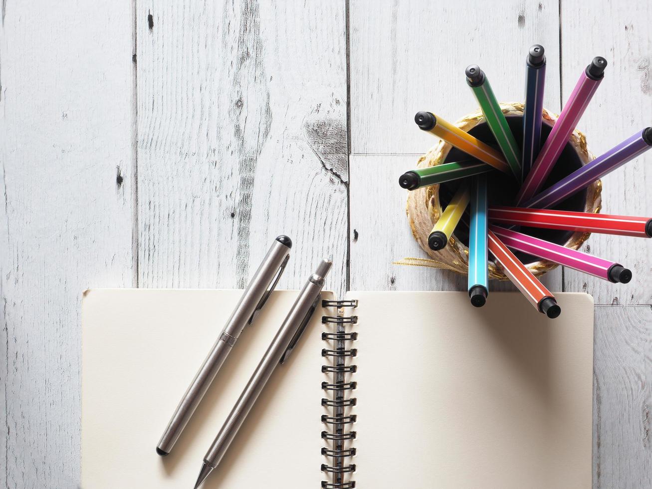 penna colorato Vettore circolare nel scatola con Aperto taccuino vuoto con Due argento penna su bianca legna tavolo e natura leggero di sole idea concetto superiore vista, affari e formazione scolastica foto