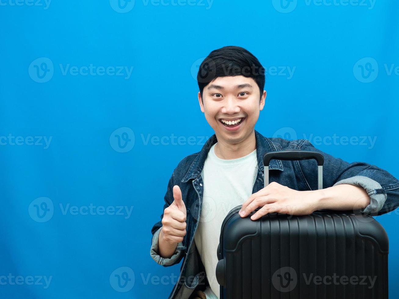 asiatico uomo sorridente con bagaglio pollice su sorridente blu sfondo foto