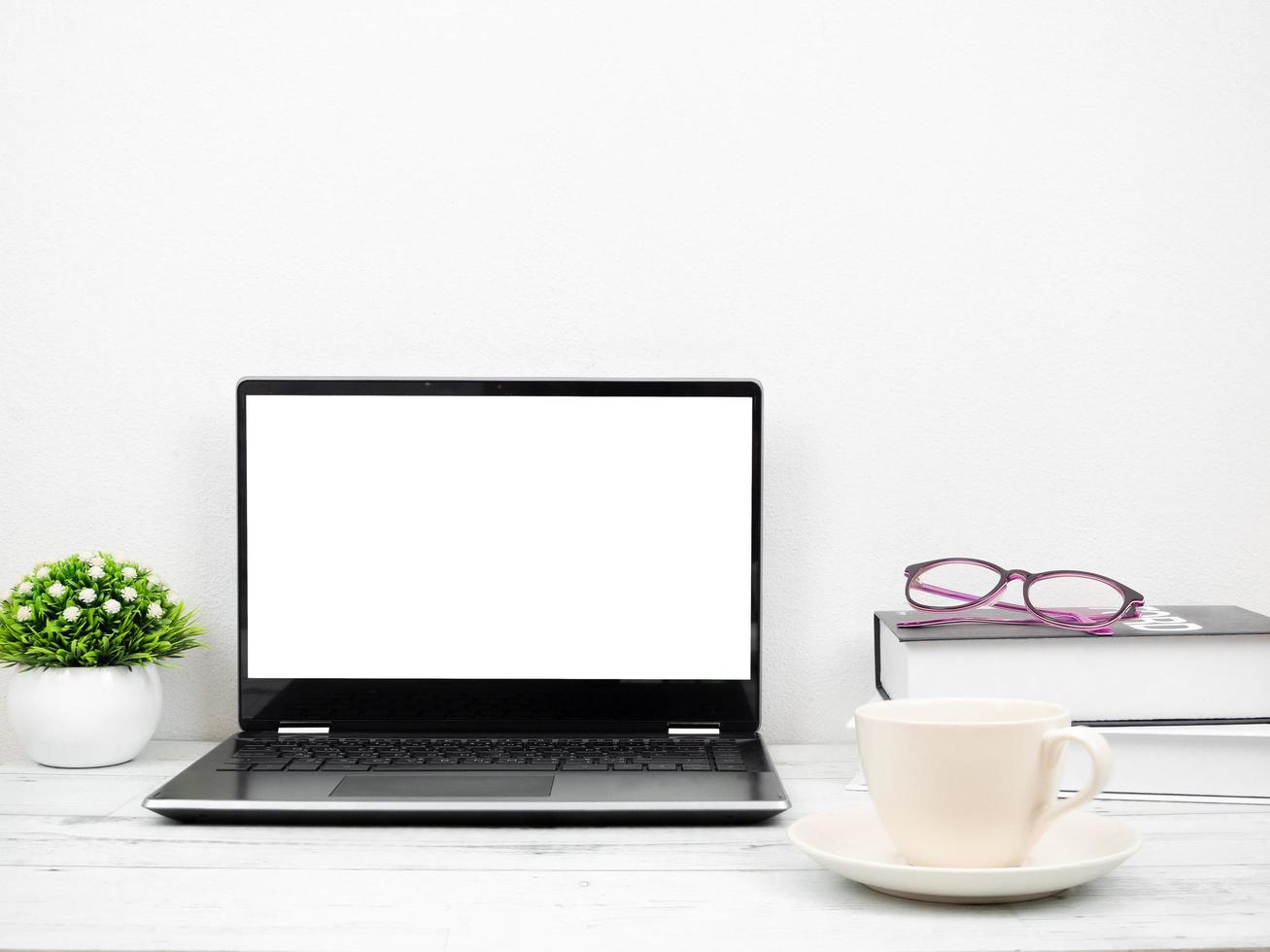 il computer portatile su il scrivania con caffè tazza libro e bicchieri spazio di lavoro a casa foto