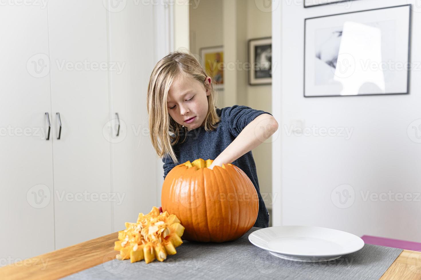 bellissimo biondo ragazzo intaglio zucca con coltello per Halloween. Halloween concetto foto