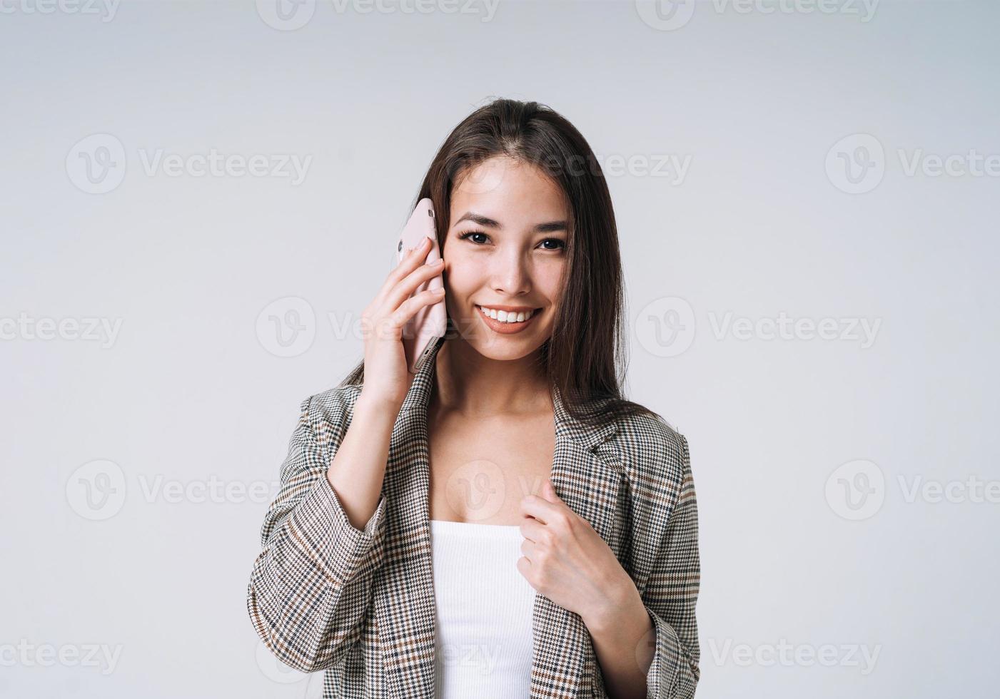 giovane contento asiatico attività commerciale donna con lungo capelli nel completo da uomo utilizzando mobile Telefono su grigio sfondo foto