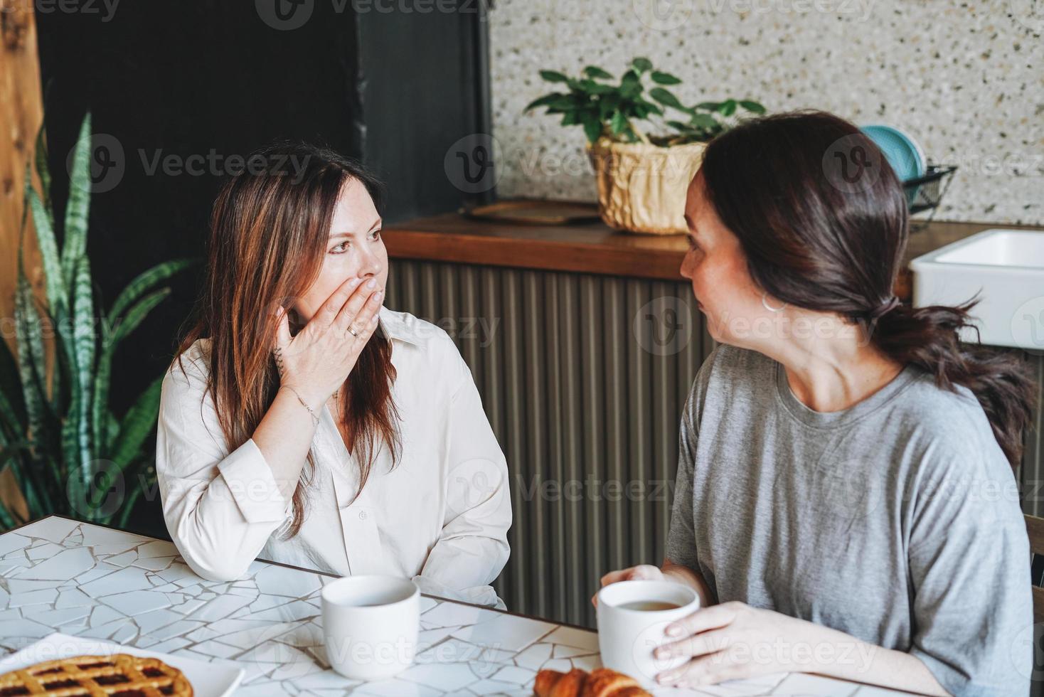 adulto sorridente brunetta mezzo anziano donne sorelle amici avendo prima colazione e comunicare nel cucina foto