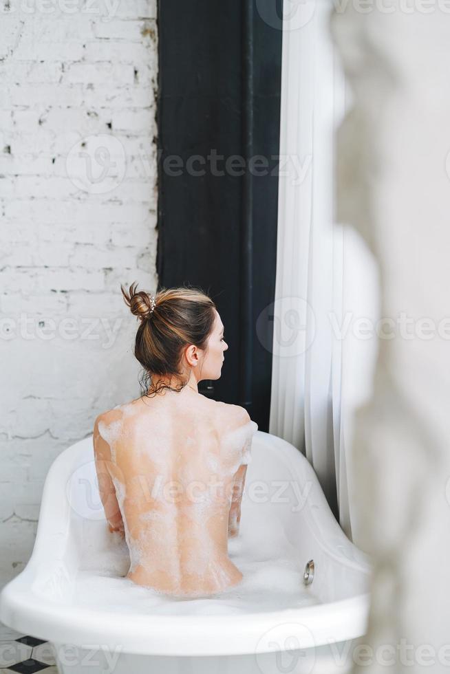 giovane contento donna assunzione bagno con schiuma a casa, trattare te stesso foto