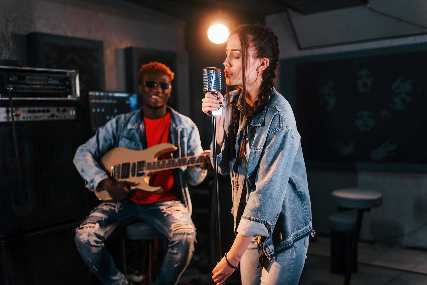 tipo giochi chitarra, ragazza canta. africano americano uomo con bianca ragazza provando nel il studio insieme foto