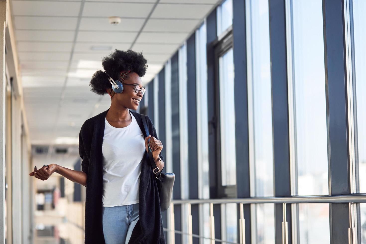 giovane africano americano femmina passanger nel casuale Abiti è nel aeroporto ascoltando musica nel cuffie foto