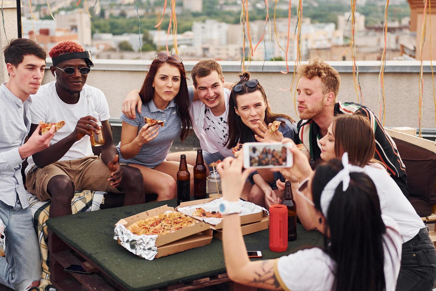 con delizioso Pizza. gruppo di giovane persone nel casuale Abiti avere un' festa a tetto insieme a giorno foto