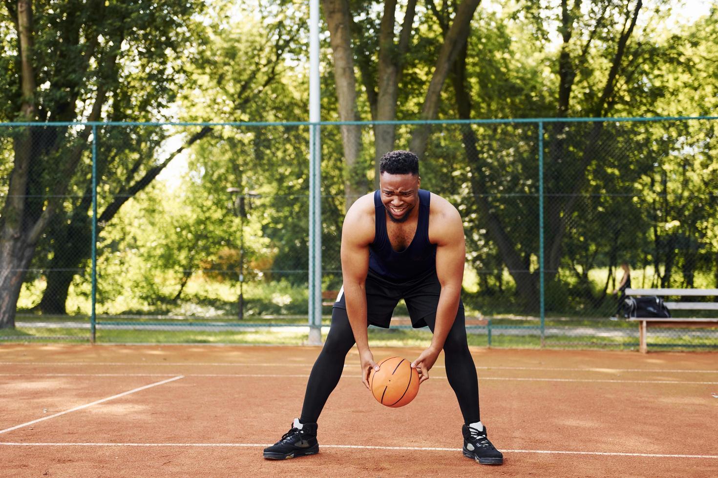 bellissimo verde alberi su sfondo. africano americano uomo giochi pallacanestro su il Tribunale all'aperto foto