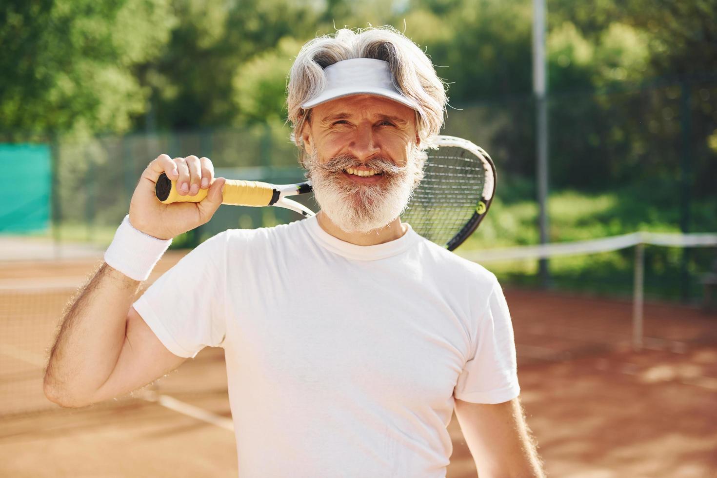 anziano moderno elegante uomo con racchetta all'aperto su tennis Tribunale a giorno foto