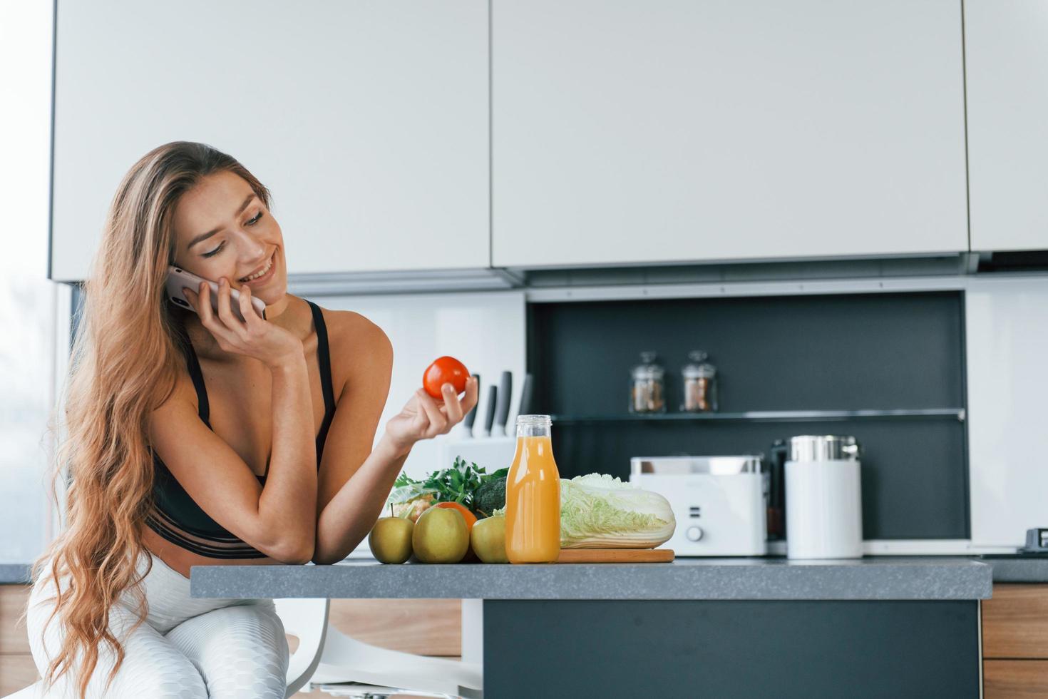 parla di il Telefono. giovane europeo donna è in casa a cucina in casa con salutare cibo foto