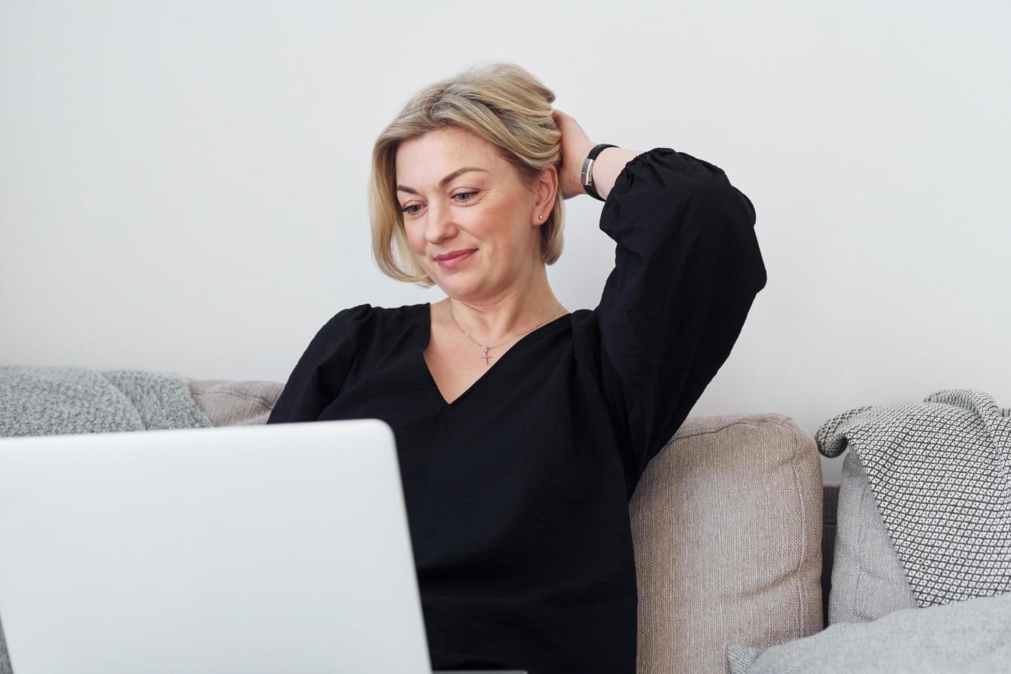 di mezza età donna nel elegante Abiti è a casa con il computer portatile foto