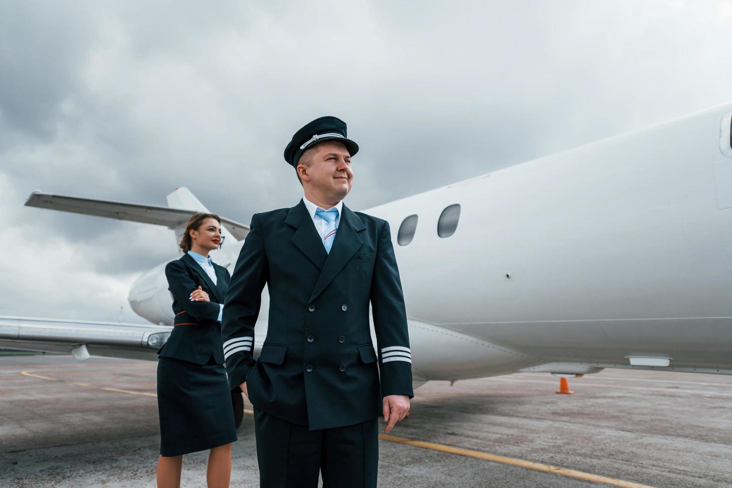 uomo con donna. aereo equipaggio nel opera uniforme è insieme all'aperto vicino aereo foto