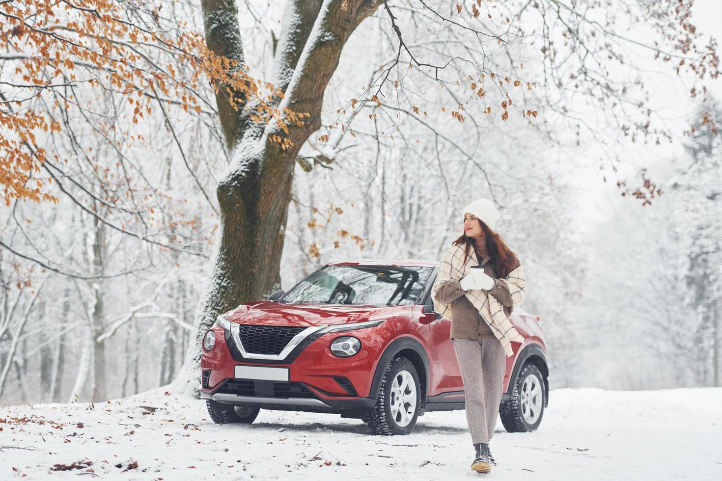 rurale scena. bellissimo giovane donna è all'aperto vicino sua rosso automobile a inverno tempo foto